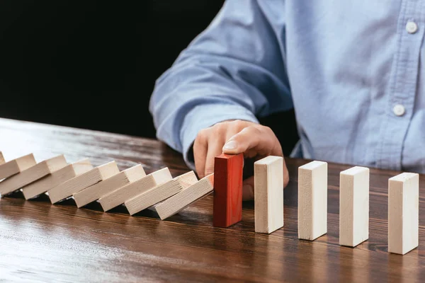 Partial view of man touching red brick and preventing wooden blocks from falling — Stock Photo