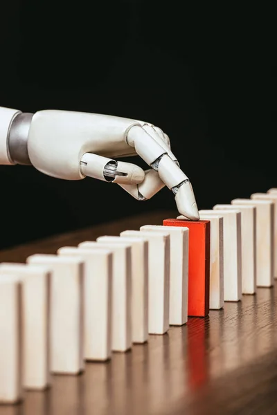 Robotic hand picking red wooden brick from row of blocks on desk isolated on black — Stock Photo