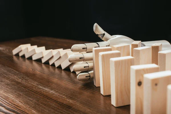 Robotic hand preventing wooden blocks from falling on desk isolated on black — Stock Photo