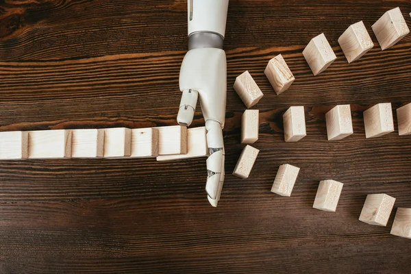 Vista superior de la mano robótica evitando que los bloques de madera caigan sobre el escritorio - foto de stock