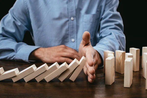 Partial view of man preventing wooden blocks from falling on desk — Stock Photo