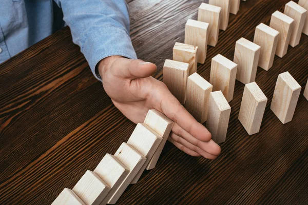 Partial view of man preventing wooden blocks from falling on desk — Stock Photo