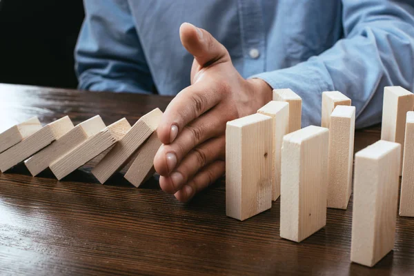 Cropped view of man preventing wooden blocks from falling on desk — Stock Photo