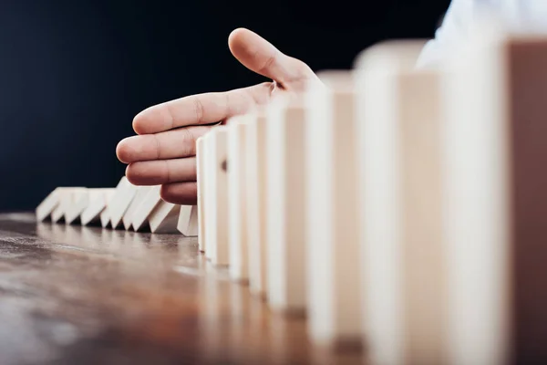 Selective focus of man preventing wooden blocks from falling on desk isolated on black — Stock Photo