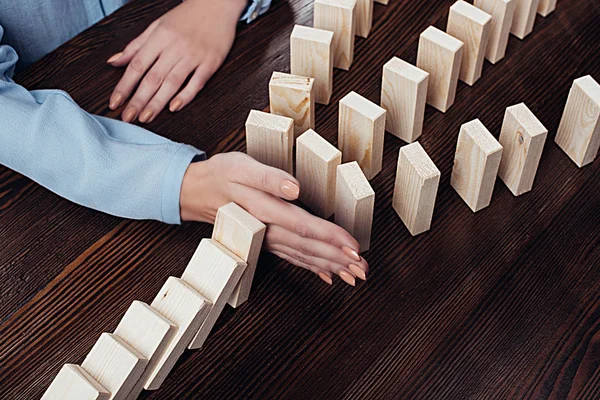 Partial view of woman sitting at table and preventing wooden blocks from falling — Stock Photo