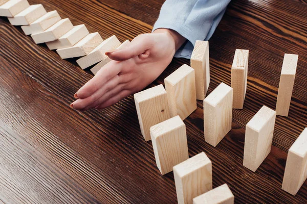Partial view of woman preventing wooden blocks from falling at desk — Stock Photo