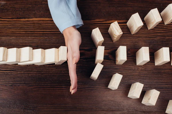 Cropped view of woman preventing wooden blocks from falling at desk — Stock Photo