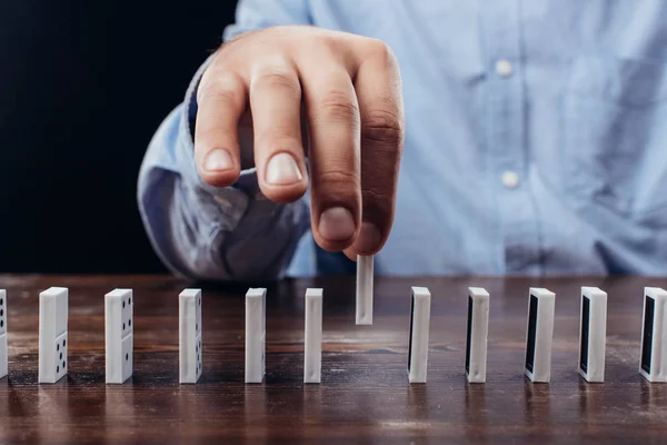 Vue partielle de l'homme ramassant domino de rangée sur le bureau isolé sur noir — Photo de stock