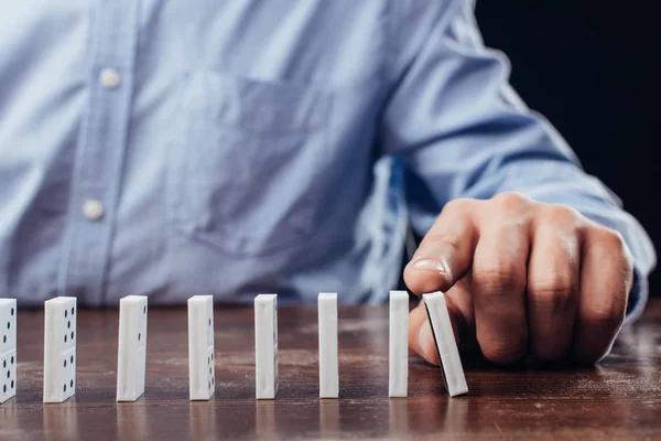 Teilansicht eines Mannes, der Domino-Reihe auf Holztisch schiebt — Stockfoto