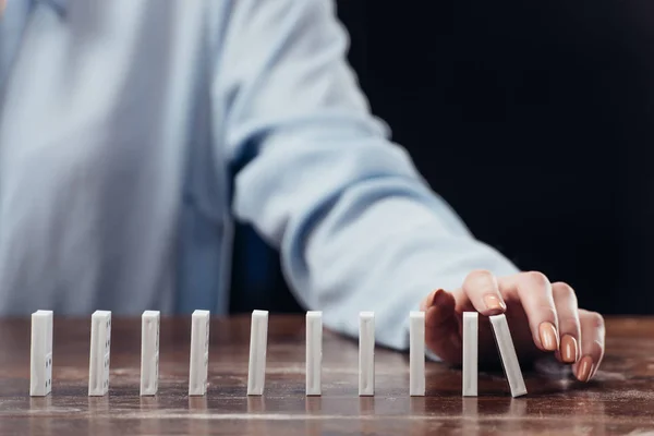 Cropped view of woman pushing domino row on wooden desk — Stock Photo