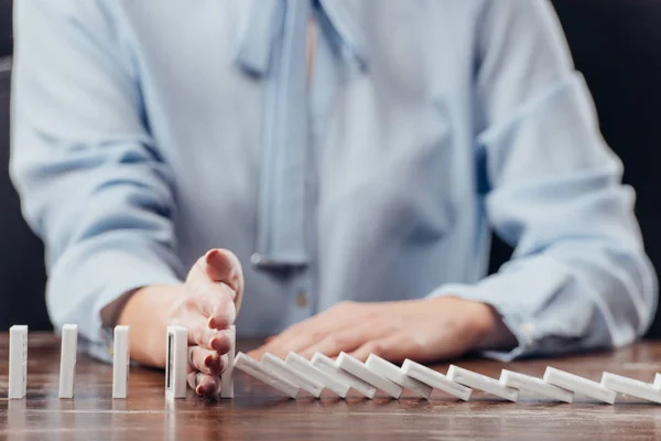 Partial view of woman preventing dominoes from falling — Stock Photo