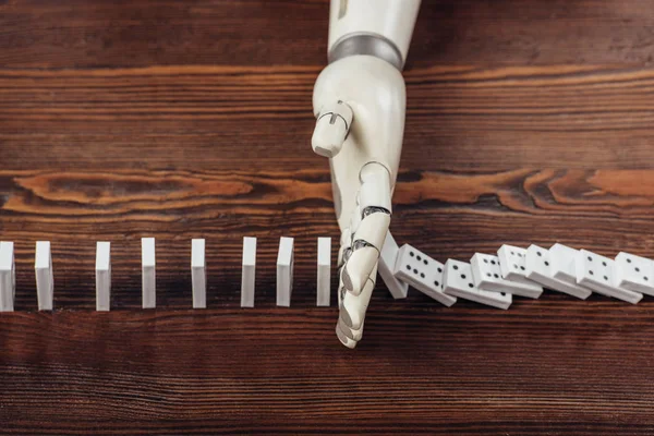 Top view of robotic hand preventing dominoes from falling on wooden desk — Stock Photo