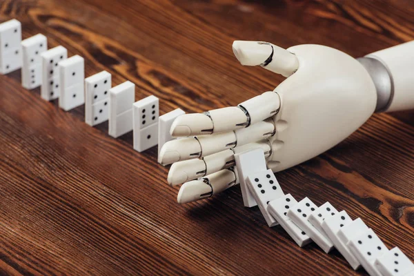 Selective focus of robotic hand preventing dominoes from falling on wooden desk — Stock Photo