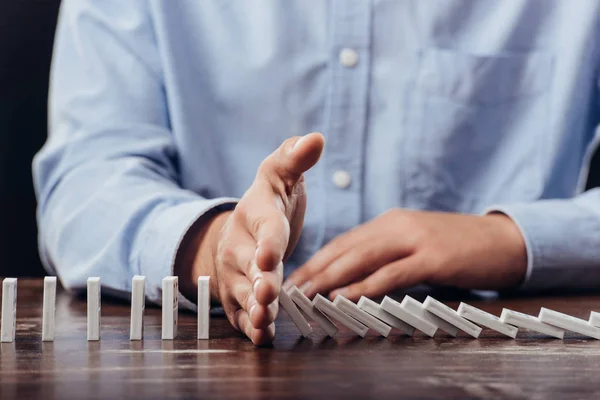 Teilansicht des Menschen verhindert, dass Dominosteine auf Schreibtisch fallen — Stockfoto