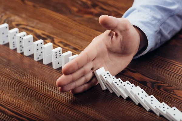 Partial view of man preventing dominoes from falling on wooden desk — Stock Photo