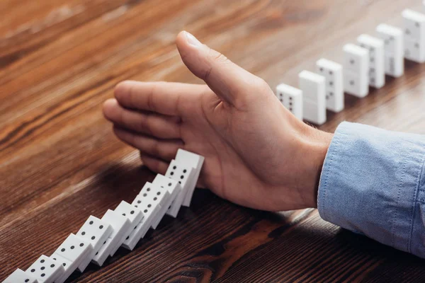 Close up view of man preventing dominoes from falling on wooden desk — Stock Photo