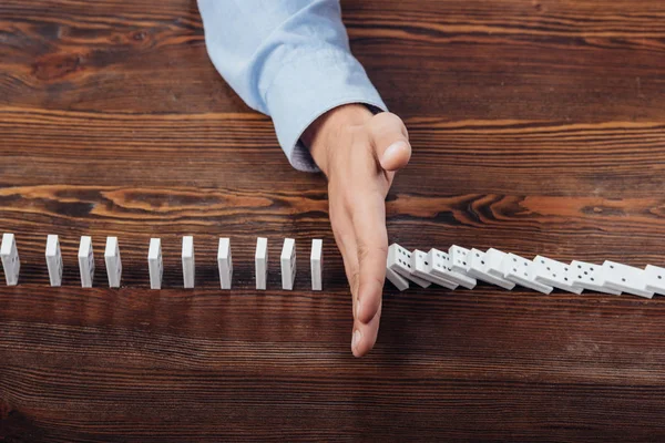 Vue de dessus de l'homme empêchant les dominos de tomber sur un bureau en bois — Photo de stock