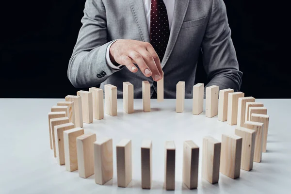 Vue partielle de l'homme ramassant la brique de bois de la rangée de blocs sur le bureau isolé sur noir — Photo de stock