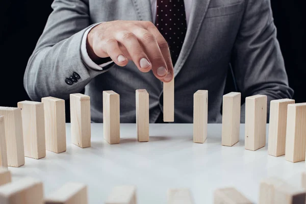 Partial view of man picking wooden brick from row of blocks on desk isolated on black — Stock Photo