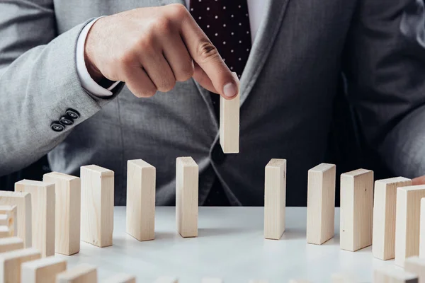 Partial view of man picking wooden brick from row of blocks on desk — Stock Photo