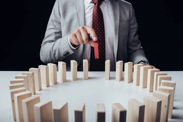 Vue partielle de l'homme d'affaires ramassant la brique rouge en bois du cercle de blocs sur le bureau isolé sur noir — Photo de stock