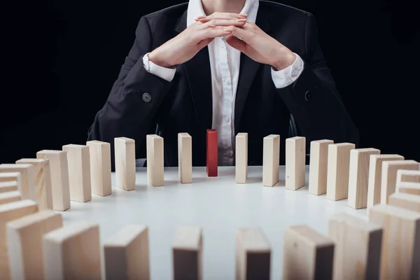 Cropped view of woman with folded hands sitting in front of circle of wooden blocks with red one isolated on black — Stock Photo