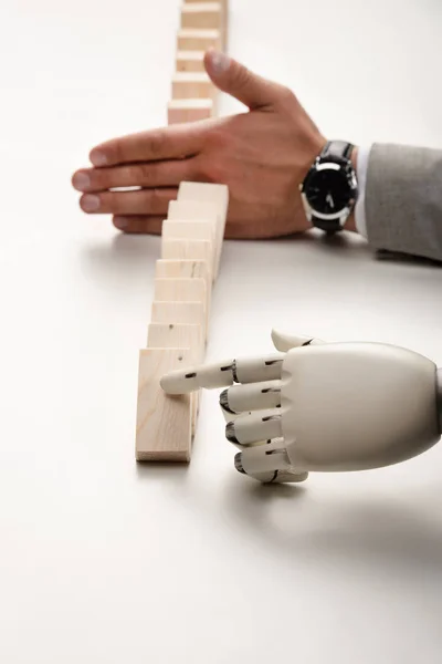 Cropped view of robotic hand pushing wooden bricks while man preventing row from falling — Stock Photo