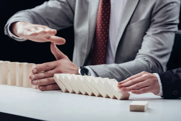 Cropped view of woman pushing wooden bricks while man preventing row from falling isolated on black — Stock Photo