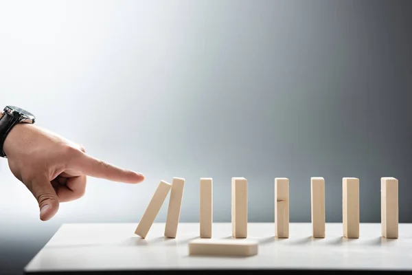 Cropped view of man pointing with finger at falling wooden block row on grey background — Stock Photo