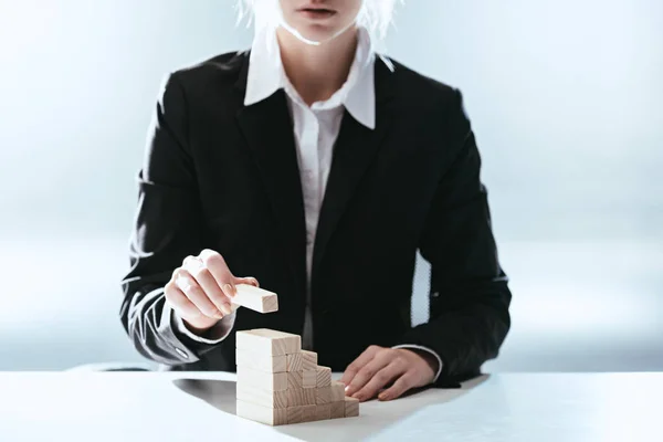 Vista recortada de la mujer poniendo ladrillo de madera en la parte superior de los bloques de madera que simbolizan la escalera de carrera con retroiluminación — Stock Photo