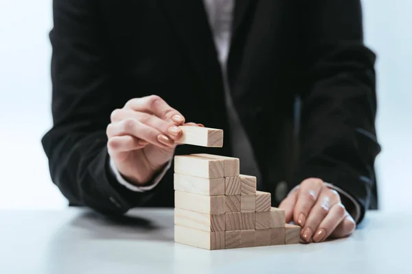 Cropped view of woman putting wooden brick on top of wooden blocks symbolizing career ladder — Stock Photo