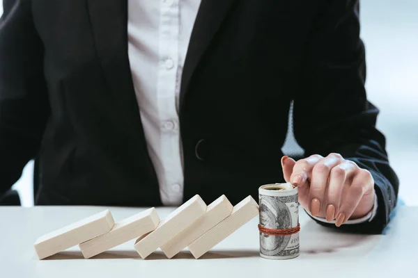 Vista parcial de la mujer de negocios sentada a la mesa con fila caída de bloques de madera y rollo de dinero - foto de stock