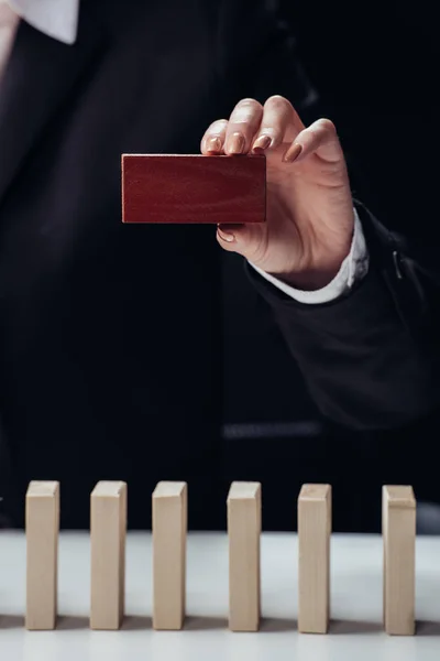 Cropped view of woman holding red brick in hand with wooden blocks on foreground isolated on black — Stock Photo