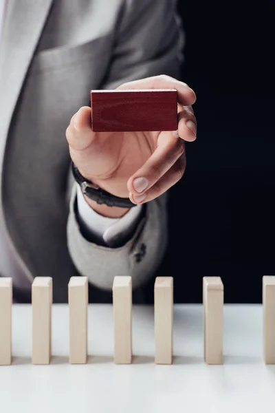 Cropped view of man holding red brick in hand with wooden blocks on foreground isolated on black — Stock Photo