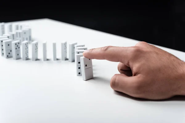 Visão parcial do homem apontando para a linha de dominó na mesa branca isolada no preto — Fotografia de Stock