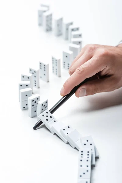 Teilansicht eines Mannes, der mit Stift auf weißem Hintergrund verhindert, dass Dominosteine fallen — Stockfoto