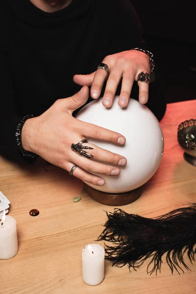 Vista ritagliata dell'uomo con anelli sulle mani sopra la sfera di cristallo sul tavolo di legno — Foto stock