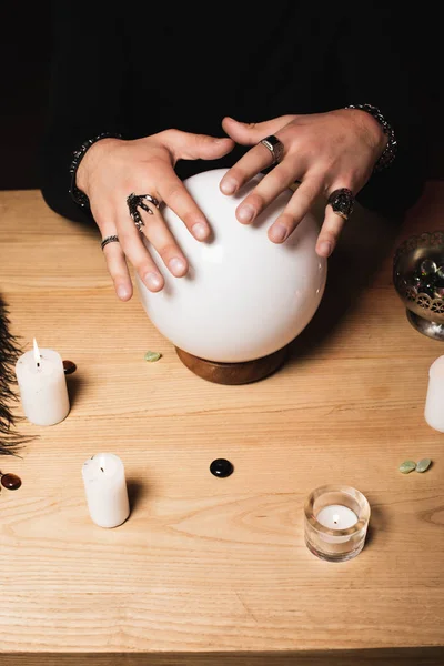 Cropped view of esoteric with rings on hands above crystal ball near candles — Stock Photo