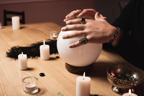 Vista ritagliata di tenuta psichica mani sopra sfera di cristallo magico vicino candele — Foto stock