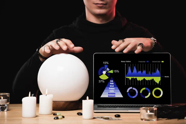 Cropped view of esoteric near laptop with charts and graphs on screen isolated on black — Stock Photo