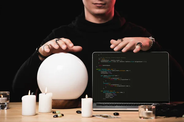 Cropped view of psychic near laptop with programming code on screen isolated on black — Stock Photo