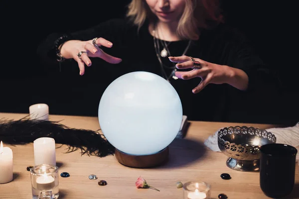 Cropped view of female esoteric holding hands above crystal ball isolated on black — Stock Photo