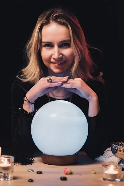 Atraente esotérico de mãos dadas acima bola de cristal perto de velas isoladas em preto — Fotografia de Stock