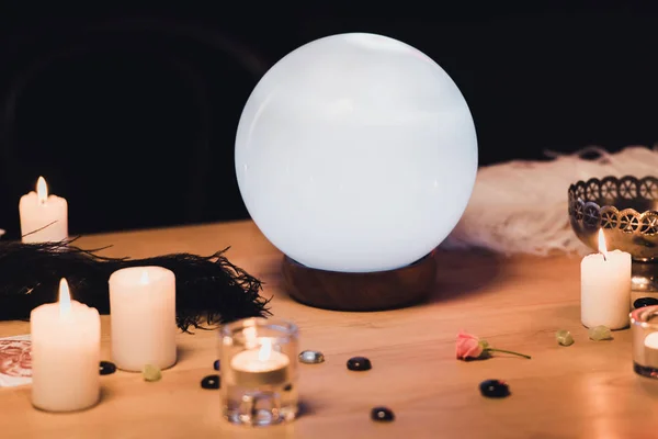 Bola de cristal perto de velas e penas em mesa de madeira isolada em preto — Fotografia de Stock