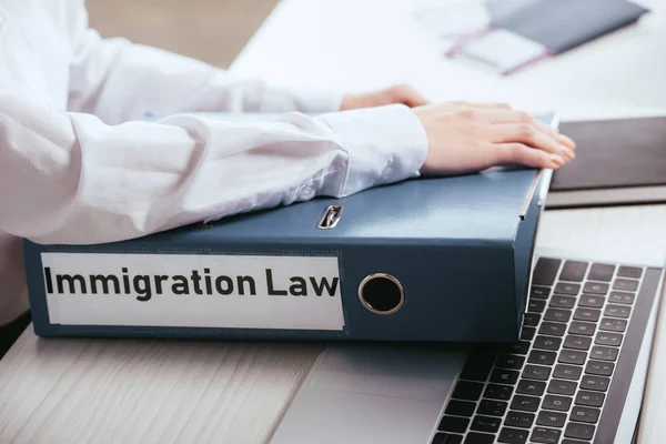 Enfoque selectivo de la mujer tomando carpeta con letras de la ley de inmigración cerca de la computadora portátil - foto de stock