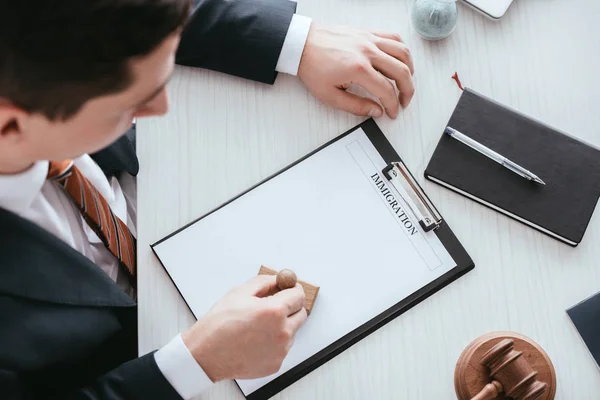 Overhead view of man in suit putting stamp on document with immigration lettering — Stock Photo