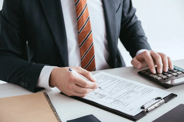 Abgeschnittene Ansicht des Mannes, der auf Taschenrechner zählt, während er Stift in der Nähe von Dokument hält, isoliert auf Weiß — Stockfoto