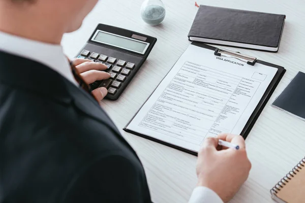 Enfoque selectivo del hombre que cuenta con la calculadora mientras sostiene la pluma cerca del documento - foto de stock