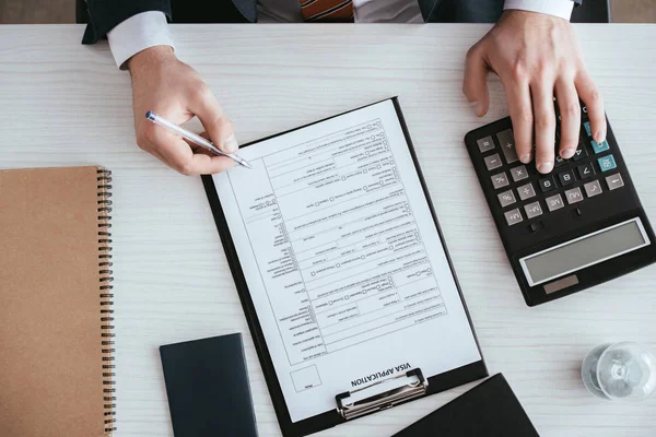 Ansicht von oben: Mann zählt auf Taschenrechner, während er Stift in Dokumentennähe hält — Stockfoto