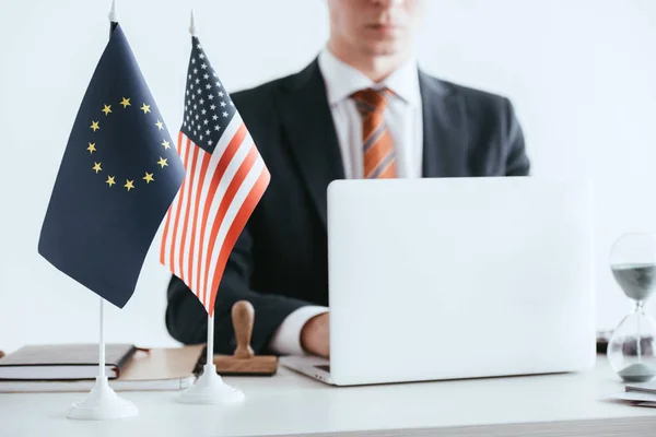 Enfoque selectivo de la computadora portátil y banderas internacionales con el hombre usando el ordenador portátil en el fondo aislado en blanco - foto de stock